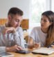Serious students discussing homework and using digital devices. Young man and woman using calculator and smartphone and sitting at desk in classroom or library. Education and friendship concept.